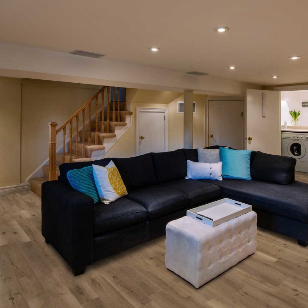 Basement with a black sectional and colorful pillows on light brown floors