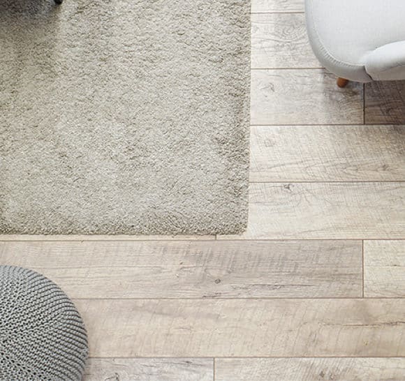 Laminate flooring with a grey knit ottoman cream chair and cream fuzzy rug
