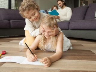 two children playing on the floor coloring as the dad sits on the couch